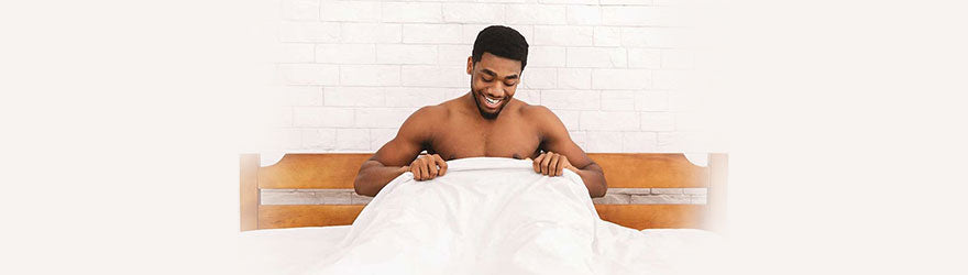 man in bed looking under the sheets