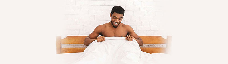 man in bed looking under the sheets